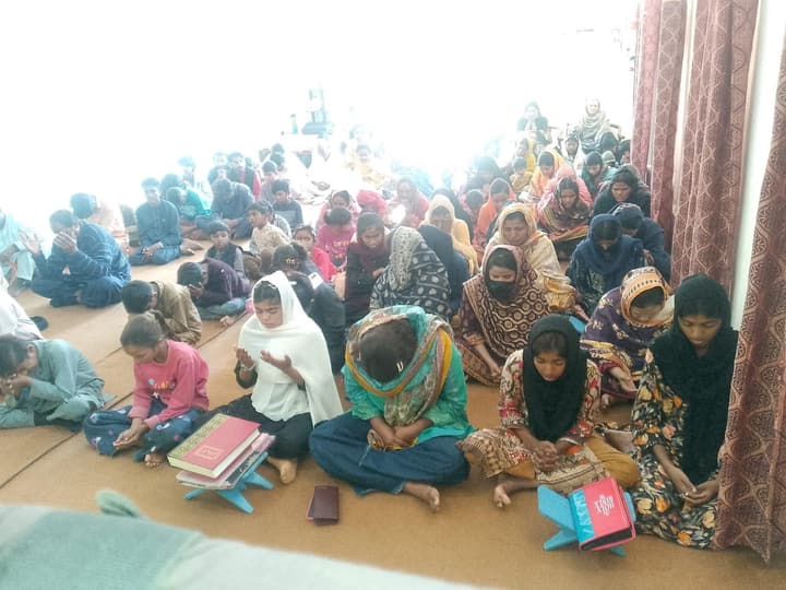 Women and children seated on the floor at a community gathering in Pakistan.
